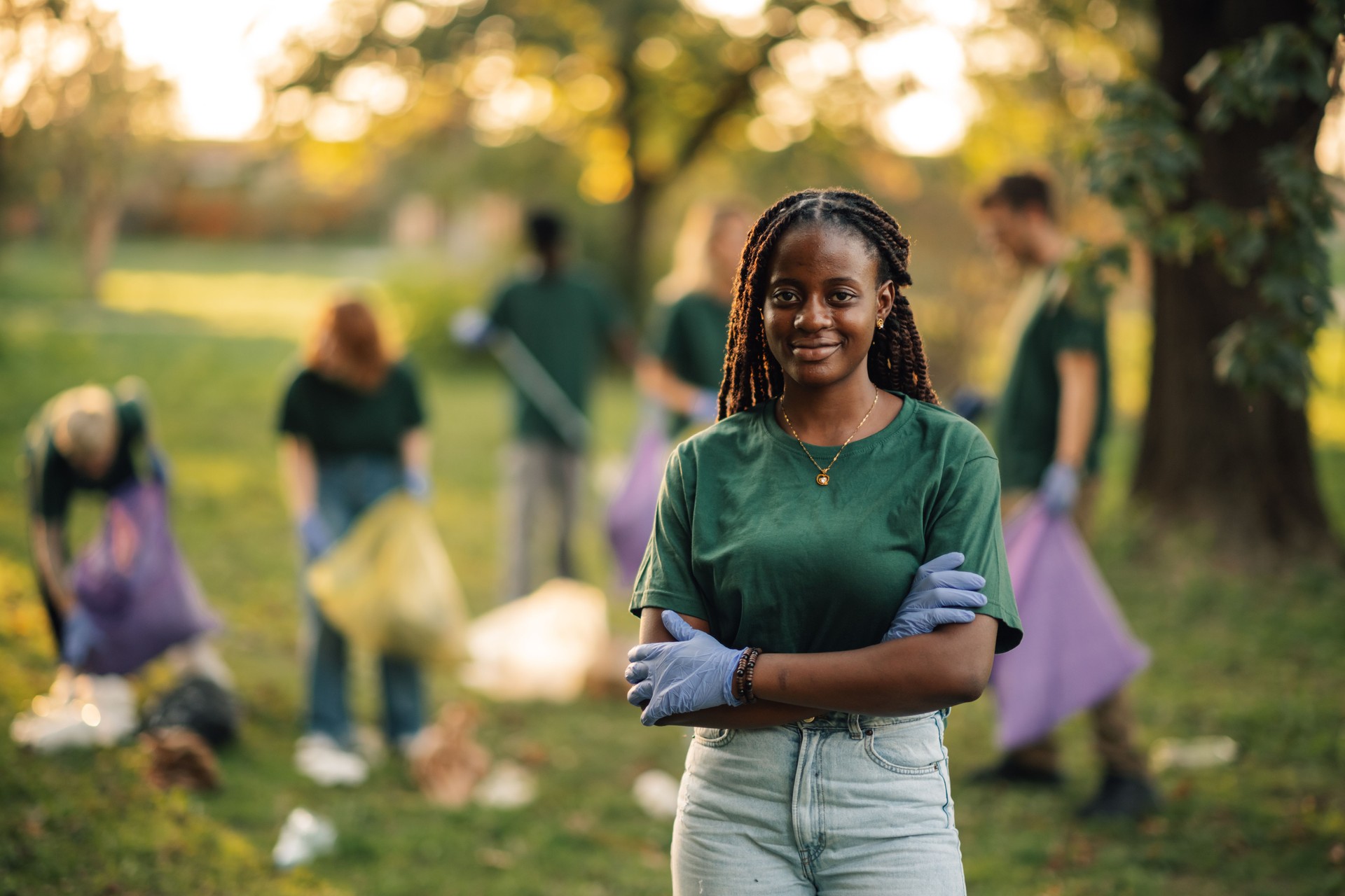 Young woman volunteer crossing arms posing with team collecting trash in park
